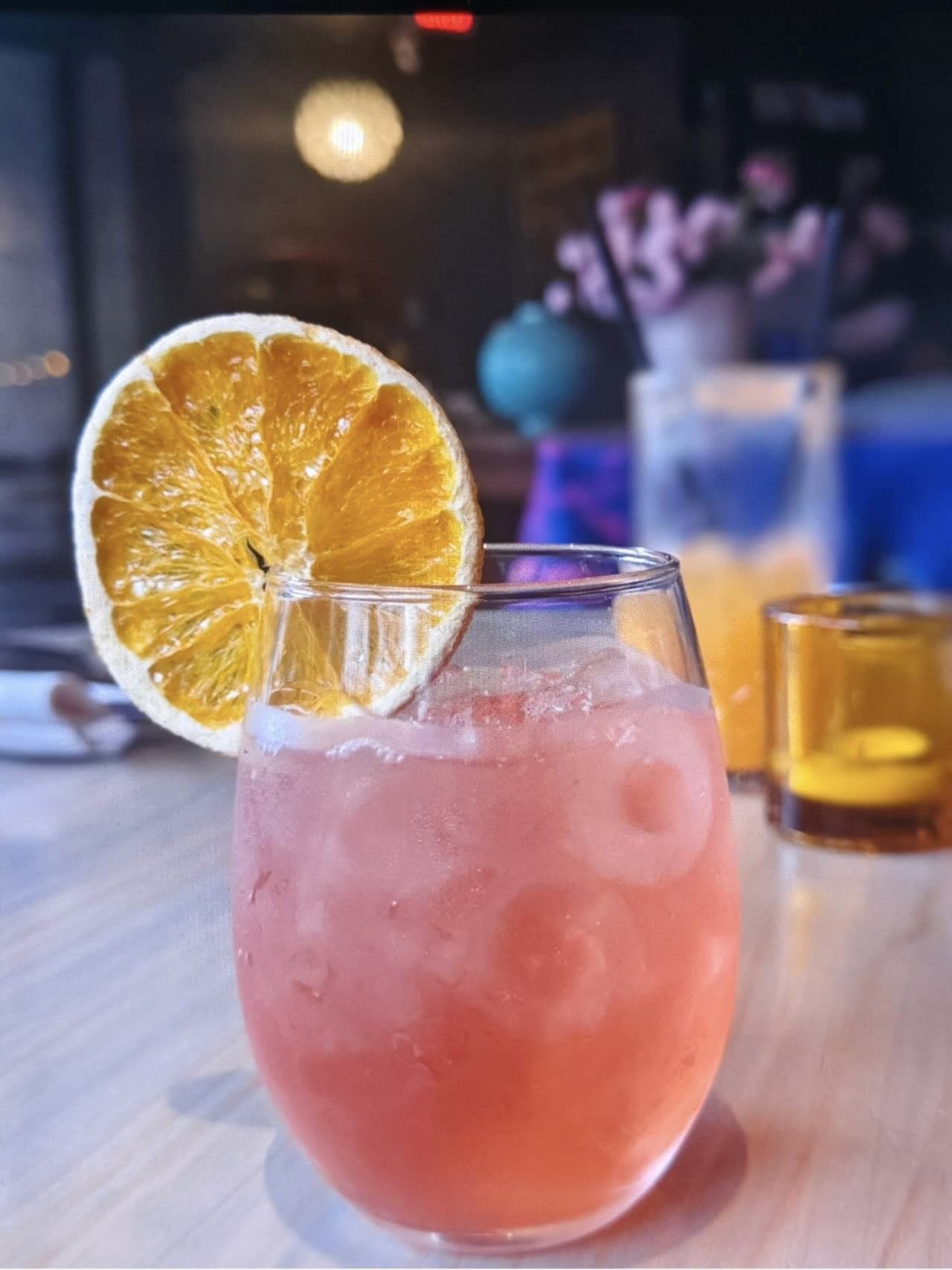 House cocktail with dried orange garnish in warm bar lighting